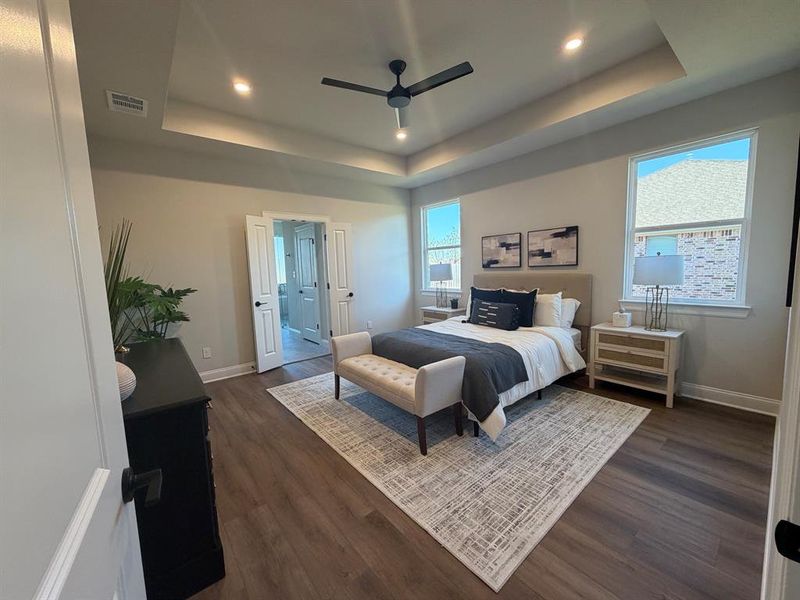 Bedroom with dark wood-type flooring, recessed lighting, ceiling fan, multiple windows, and a raised ceiling