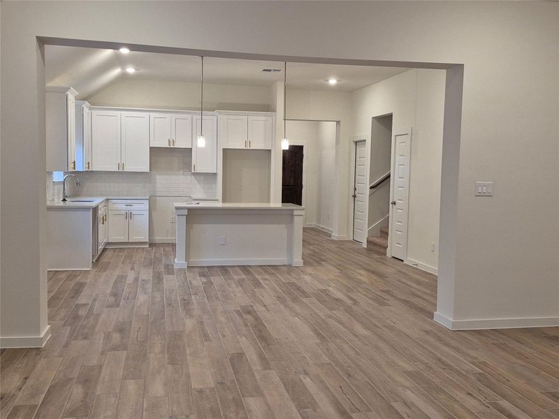 Spacious open-concept kitchen with modern white cabinetry, elegant pendant lighting, and stylish wood-look flooring, perfect for entertaining.