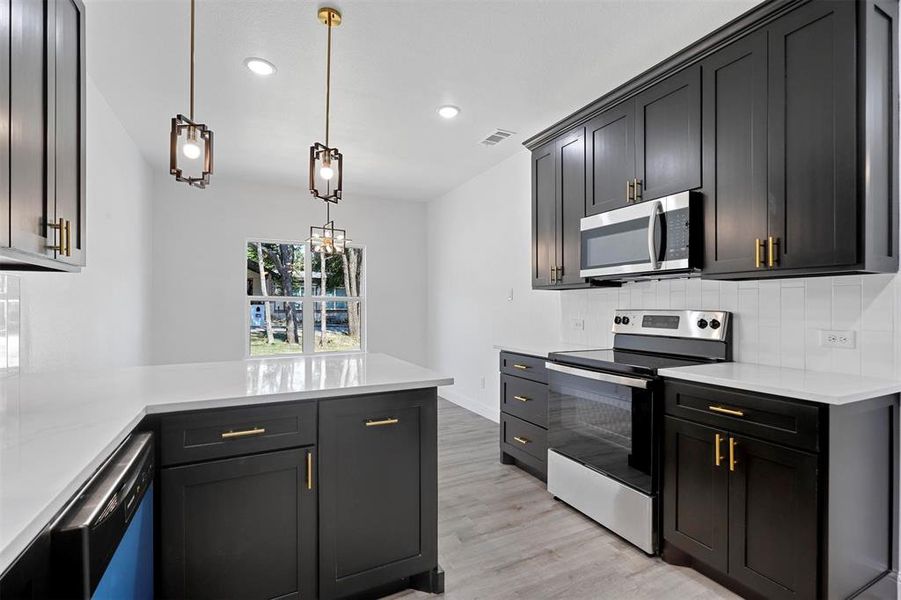 Kitchen featuring stainless steel appliances, light hardwood / wood-style flooring, tasteful backsplash, and pendant lighting