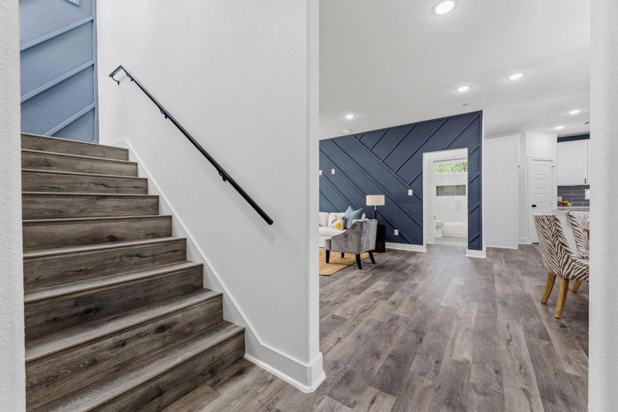 Hardwood stairs ascend gracefully, connecting to an open-concept living space with a distinct accent wall.