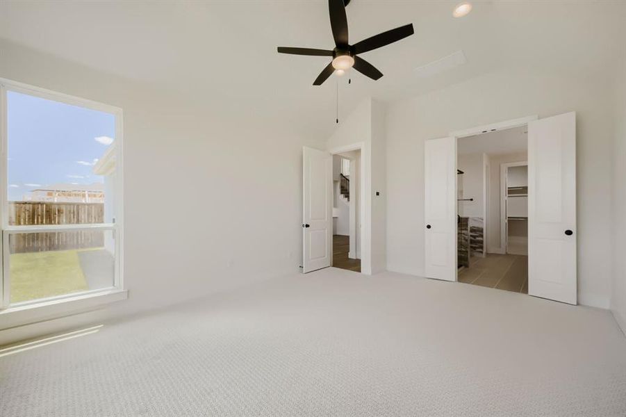 Carpeted room featuring a ceiling fan with light, a large window, and double doors opening to a separate space with tiled flooring