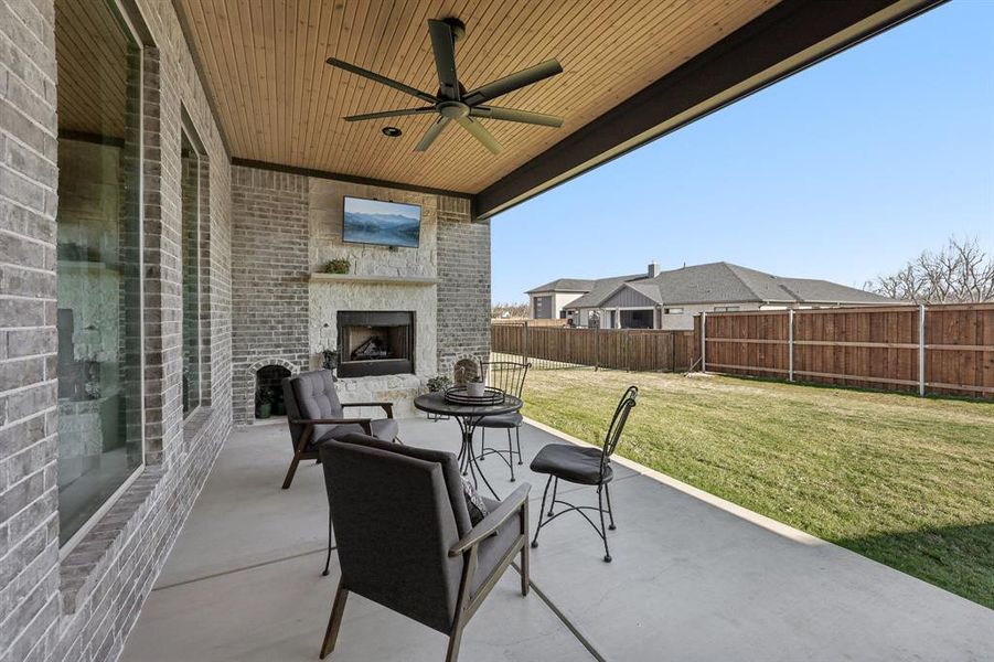 Fenced backyard featuring a large fireplace, a ceiling fan, and a patio Fenced backyard featuring a large fireplace, a ceiling fan, and a patio