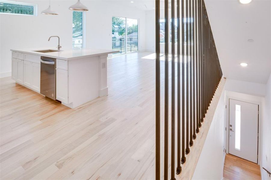 Kitchen featuring sink, white cabinetry, stainless steel dishwasher, pendant lighting, and light hardwood / wood-style flooring