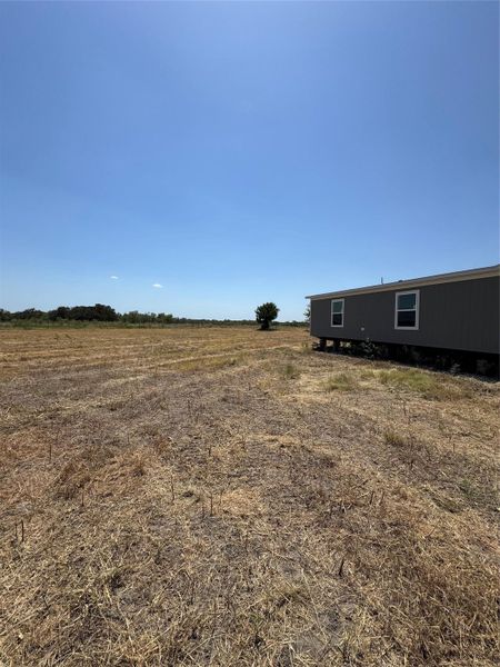 An expansive clearing borders the structured profile of this rural residence under wide blue skies.