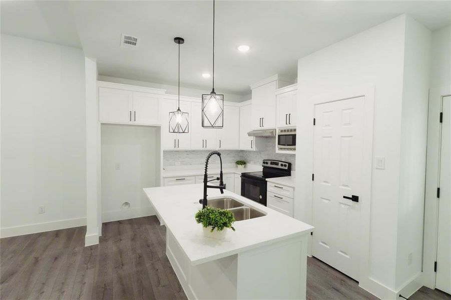 Kitchen with electric range oven, stainless steel microwave, dark wood finished floors, tasteful backsplash, and an island with sink Kitchen with electric range oven, stainless steel microwave, dark wood finished floors, tasteful backsplash, and an island with sink