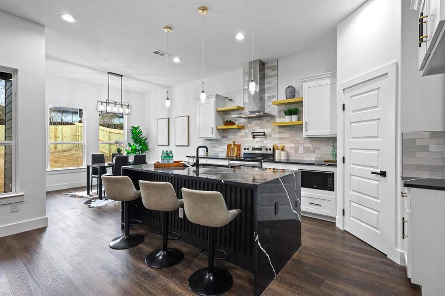 Kitchen featuring wall chimney exhaust hood, a kitchen bar, decorative light fixtures, a center island with sink, and white cabinets