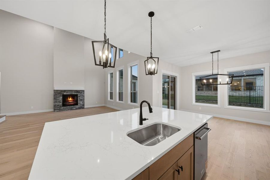 Kitchen with hanging light fixtures, light wood-style floors, a fireplace, and light stone counters