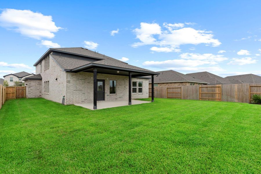 A wide view of the backyard highlights the home’s full brick exterior, extended patio, and spacious lawn—ideal for play, pets, or future outdoor upgrades.