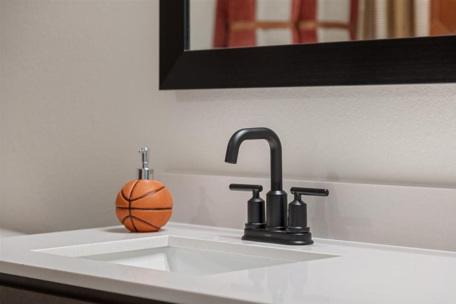 Secondary bath features tile flooring, bath/shower combo with tile surround, extended cabinet with knee space, beautiful light countertops, black framed mirror, sleek black fixtures and modern finishes.