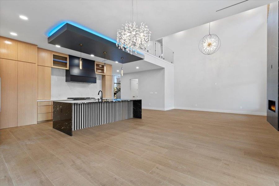 Kitchen featuring modern cabinets, hanging light fixtures, light wood cabinetry, a kitchen island with sink, and custom range hood Kitchen featuring modern cabinets, hanging light fixtures, light wood cabinetry, a kitchen island with sink, and custom range hood