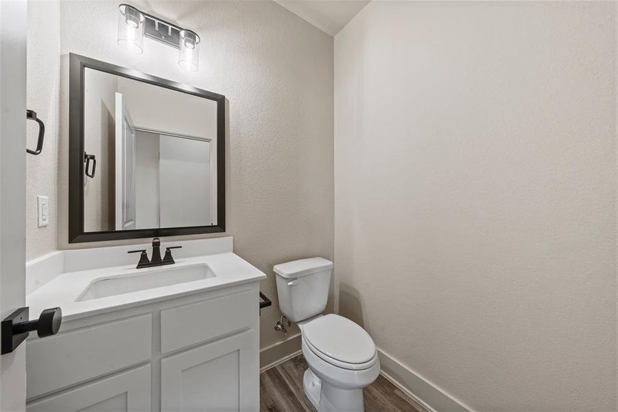 Bathroom featuring a white vanity with an integrated sink, dark bronze hardware, a framed mirror, and wood-finish flooring Bathroom featuring a white vanity with an integrated sink, dark bronze hardware, a framed mirror, and wood-finish flooring