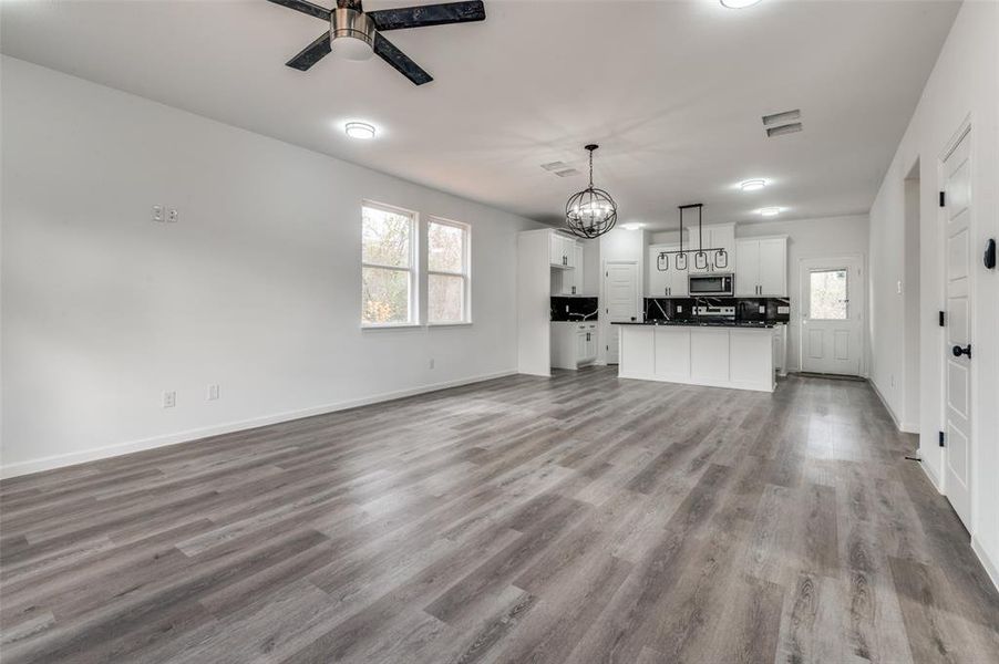 Unfurnished living room featuring ceiling fan with notable chandelier and light hardwood / wood-style flooring