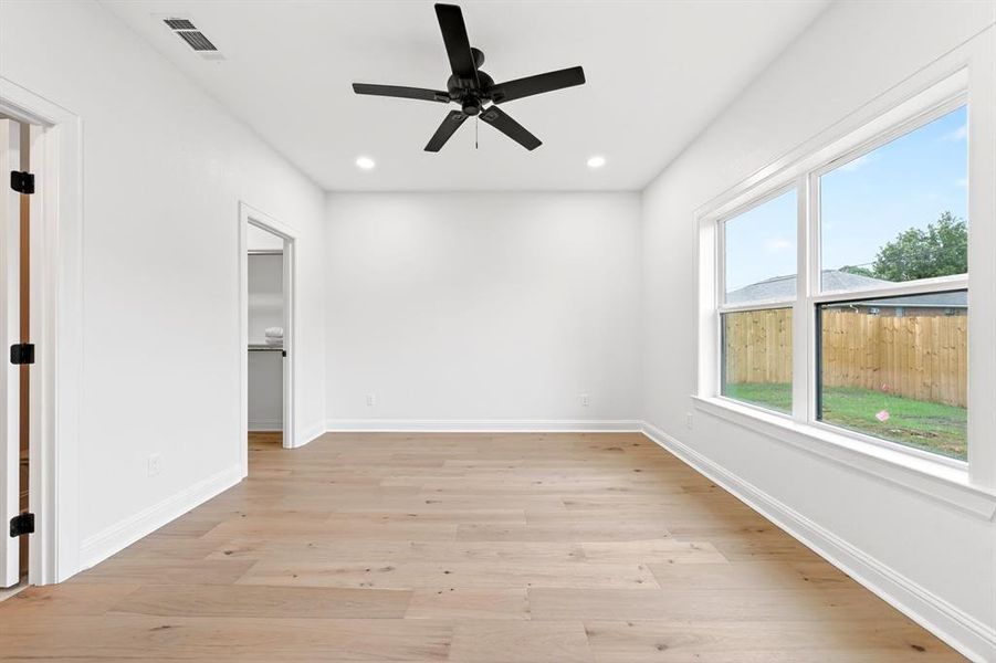 Spacious interior room featuring wood-finish flooring, a contemporary black ceiling fan, and recessed lighting