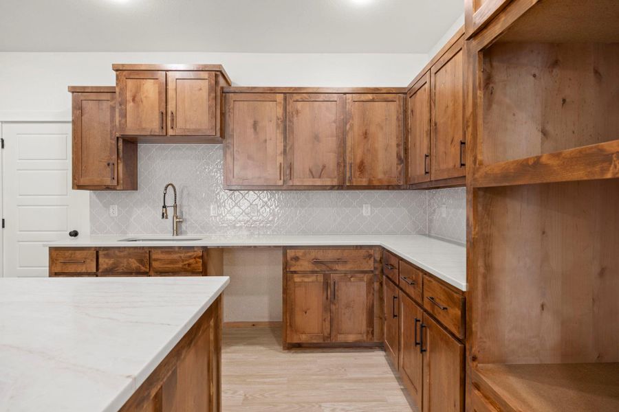A well-lit kitchen features custom wooden cabinetry and white countertops, offering ample workspace and storage.