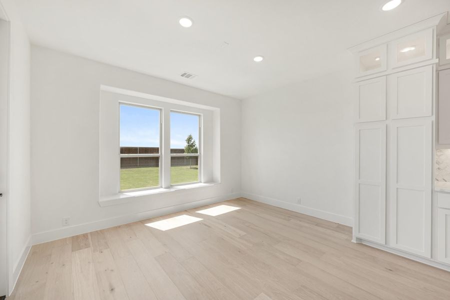 Empty room with light hardwood floors, white walls, double window, and built-in white cabinetry