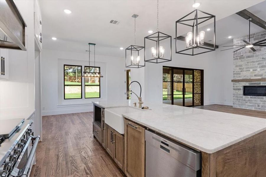 Kitchen with dark hardwood / wood-style floors, a stone fireplace, a kitchen island with sink, and appliances with stainless steel finishes