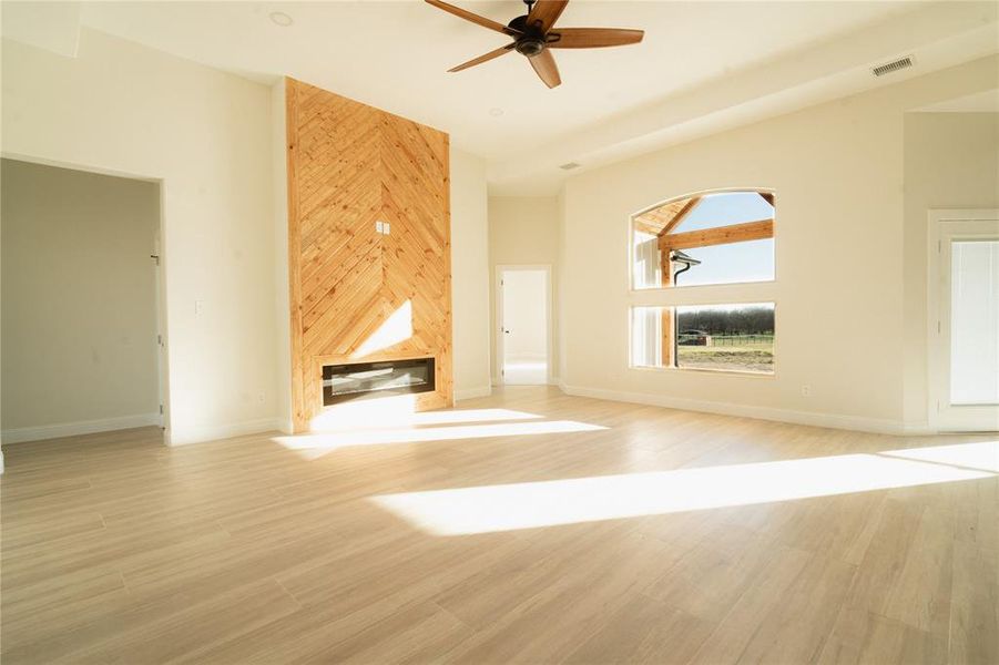 Unfurnished living room with a large fireplace, a high ceiling, light wood-type flooring, and baseboards