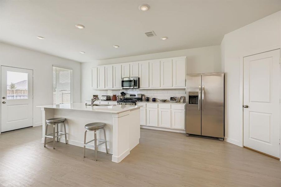 Kitchen with stainless steel appliances, decorative backsplash, a kitchen breakfast bar, white cabinets, and recessed lighting