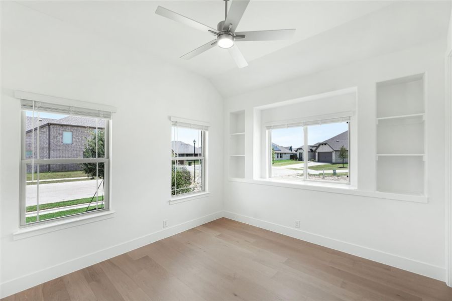 Empty bedroom with vaulted ceiling, ceiling fan, built-in shelves, and hardwood floors