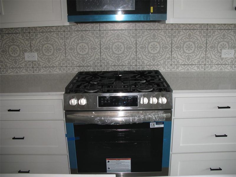 Kitchen featuring appliances with stainless steel finishes, white cabinetry, and tasteful backsplash