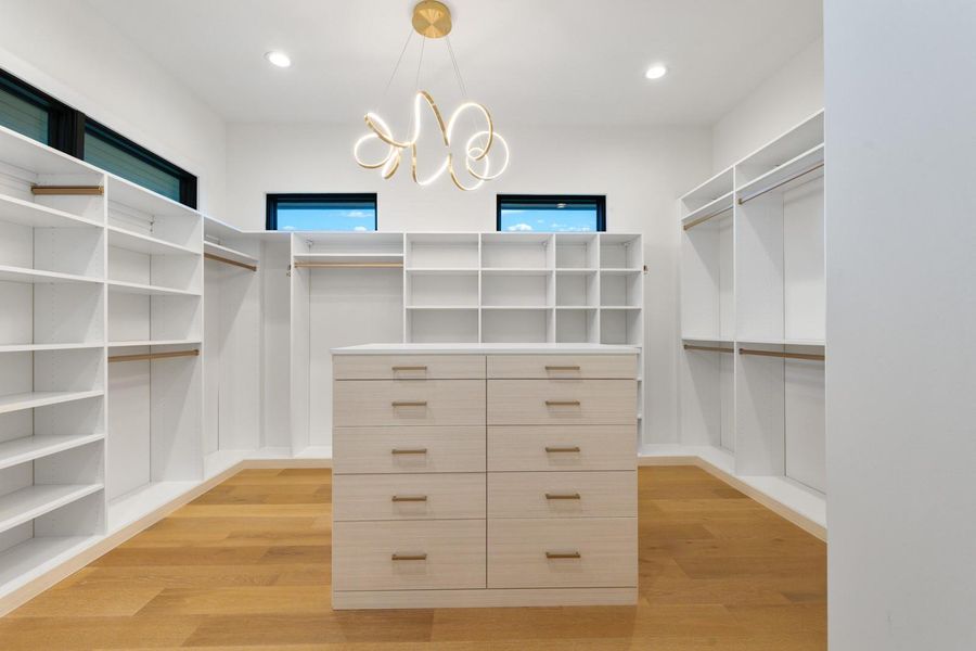 Spacious walk-in closet featuring extensive built-in shelving, hanging rods, a central island with drawers, and a decorative ceiling light fixture