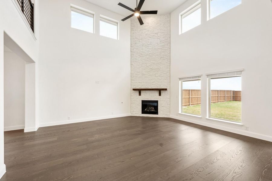 Open living room with two-story ceilings, stone fireplace, ceiling fan, and dark hardwood floors