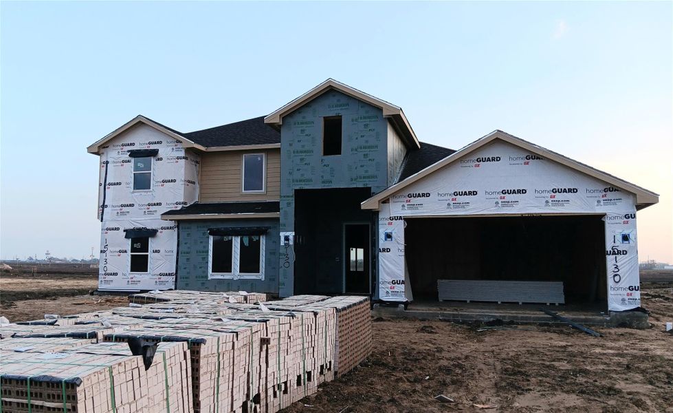 Front exterior view of a two-story new construction home currently under construction, featuring a brick and siding elevation, covered entry, and three-car garage. Materials and finishes are in progress, with masonry staged on site. Located on a spacious homesite within Riverside Estates