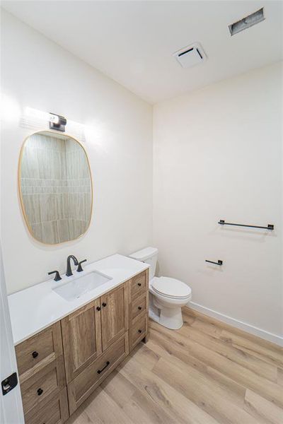 Guest Bathroom featuring a wood-finish vanity with a white countertop, an undermount sink with a matte black faucet, and wood-finish flooring