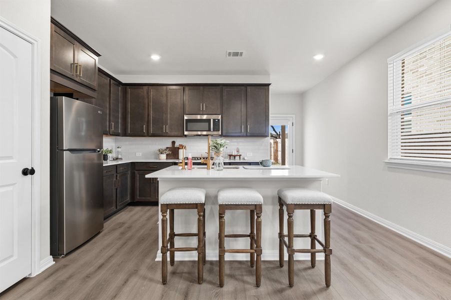 Kitchen featuring dark brown cabinetry, stainless steel appliances, an island with sink, a kitchen breakfast bar, and recessed lighting Kitchen featuring dark brown cabinetry, stainless steel appliances, an island with sink, a kitchen breakfast bar, and recessed lighting
