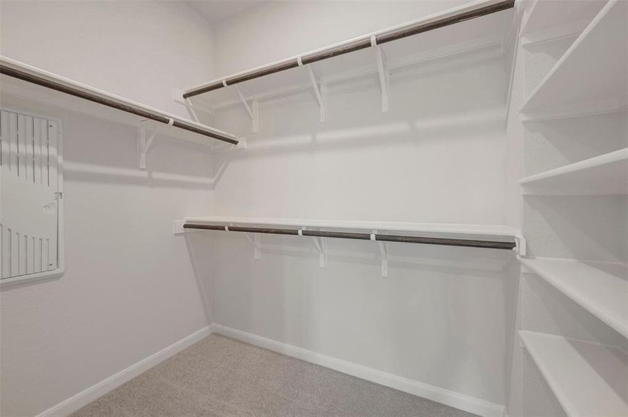 Spacious walk-in closet featuring built-in shelving, multiple hanging rods, and light-toned carpeting Spacious walk-in closet featuring built-in shelving, multiple hanging rods, and light-toned carpeting