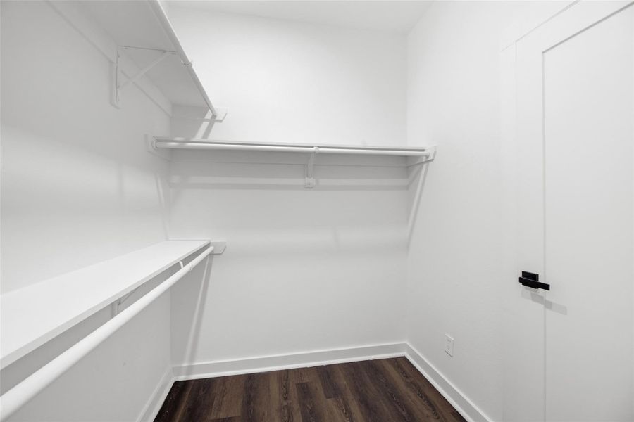 Large walk-in closet with white walls and shelving, featuring wood flooring and ample hanging space.