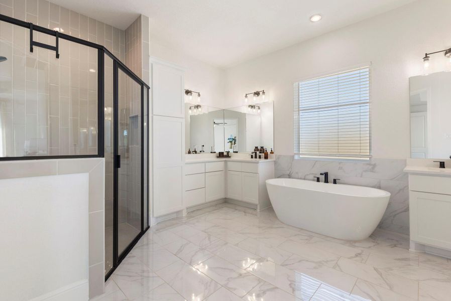 This spacious bathroom features a modern design with a freestanding bathtub, large glass-enclosed shower, dual vanities with ample storage, and elegant tile flooring. Bright and airy, it offers a luxurious retreat.