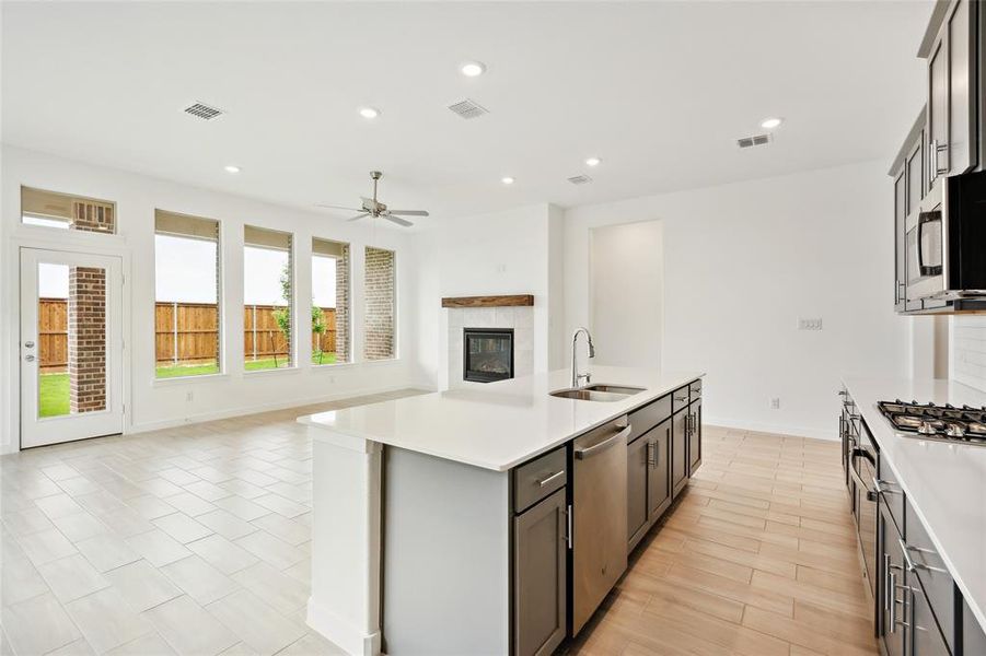 Kitchen featuring stainless steel appliances, an island with sink, a tiled fireplace, ceiling fan, and sink