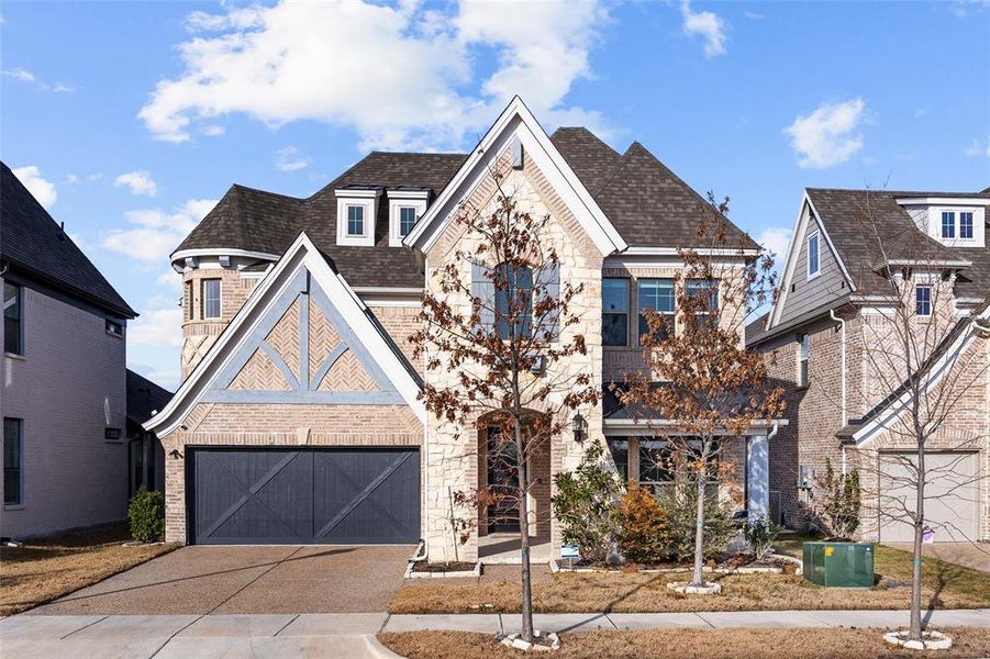 View of front of home featuring roof with shingles, stone siding, a garage, brick siding, and driveway