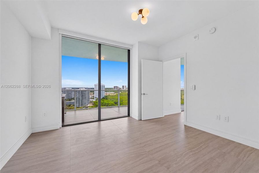 Room featuring wood-finish flooring, floor-to-ceiling glass sliding doors, a private balcony, and a modern three-globe flush-mount light fixture