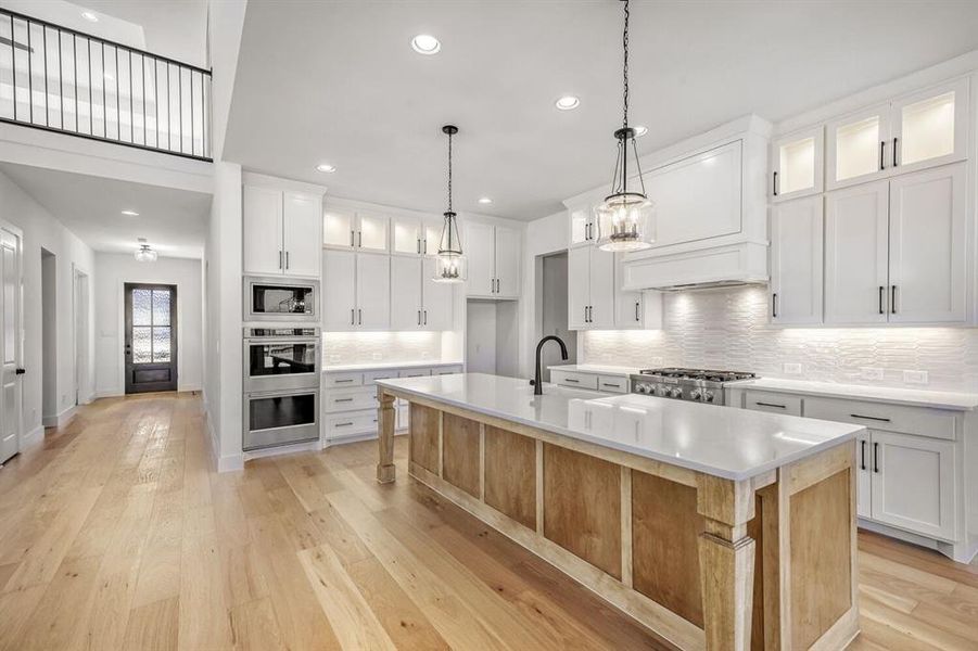 Kitchen featuring a kitchen island with sink, light wood-style floors, pendant lighting, stainless steel appliances, and backsplash