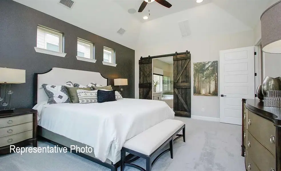 Carpeted bedroom featuring a barn door, high vaulted ceiling, ceiling fan, and multiple windows