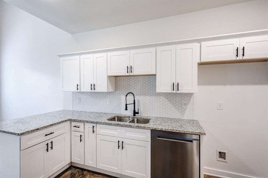 Kitchen with white cabinets, dishwasher, light stone countertops, decorative backsplash, and sink