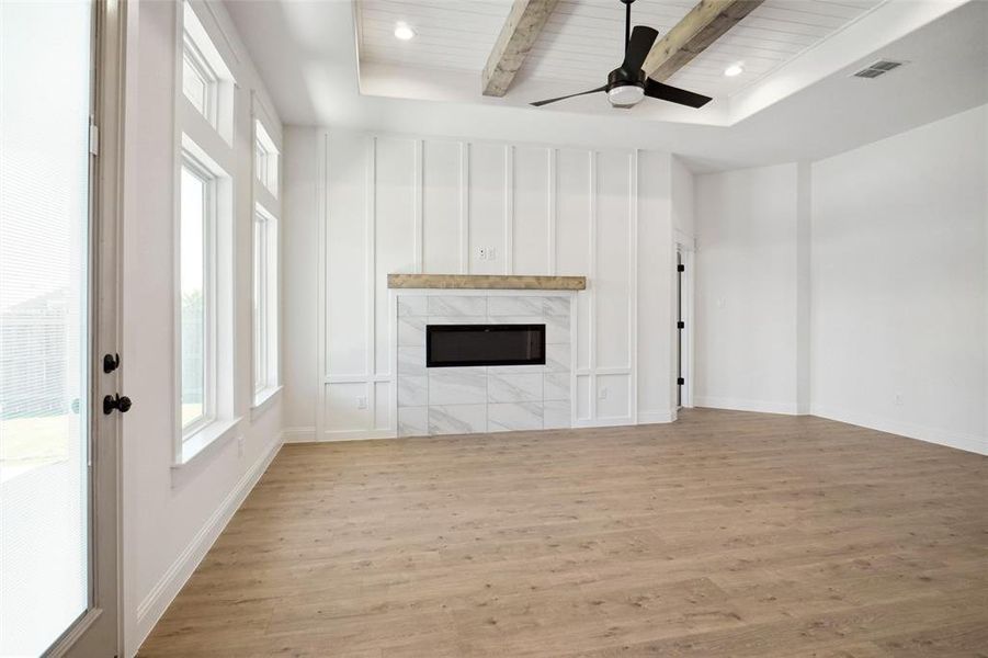 Unfurnished living room featuring a tile fireplace, ceiling fan, beamed ceiling, wood ceiling, and light wood-type flooring