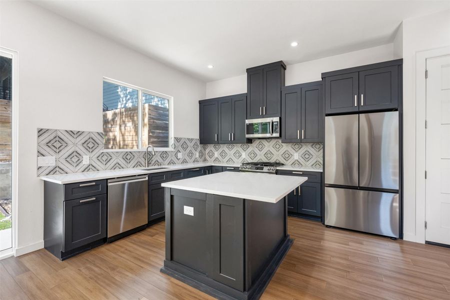 Kitchen with appliances with stainless steel finishes, backsplash, a center island, light wood finished floors, and light stone countertops