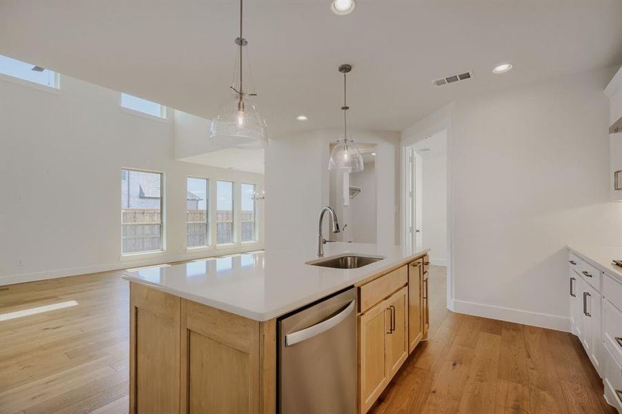 Kitchen island featuring a stainless steel sink with a gooseneck faucet, light wood cabinetry, and a light-toned countertop