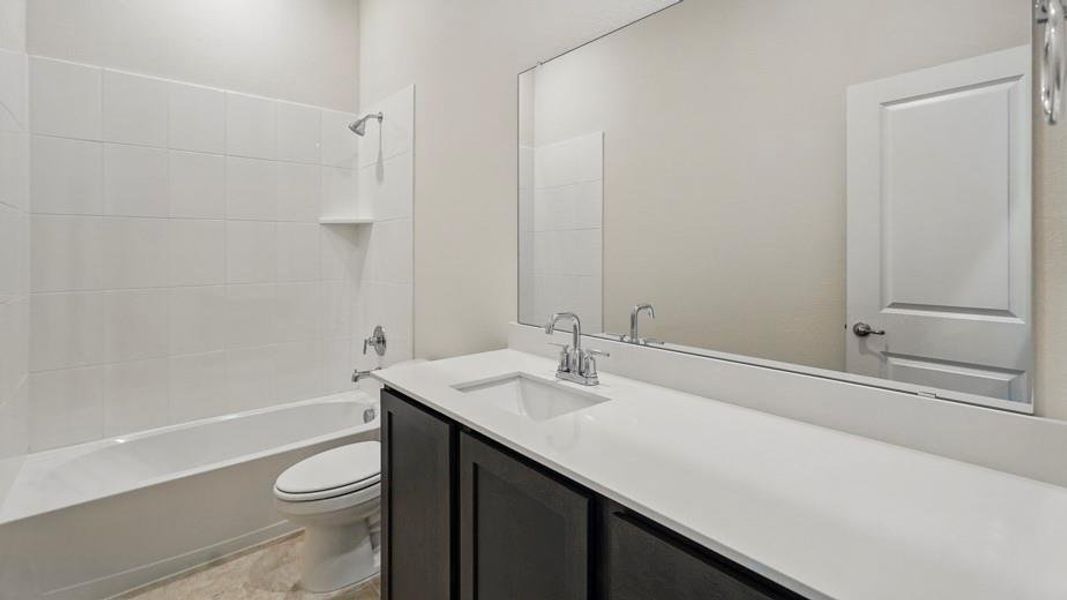 Bathroom featuring a white subway tile tub surround, dark wood-finish vanity with a white countertop, and a large wall-mounted mirror