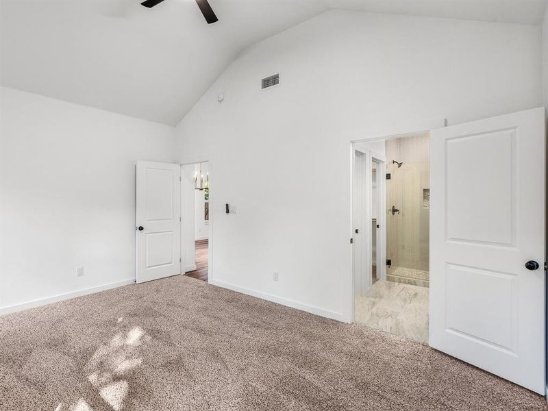 Unfurnished bedroom featuring high vaulted ceiling, carpet, a chandelier, a ceiling fan, and ensuite bath