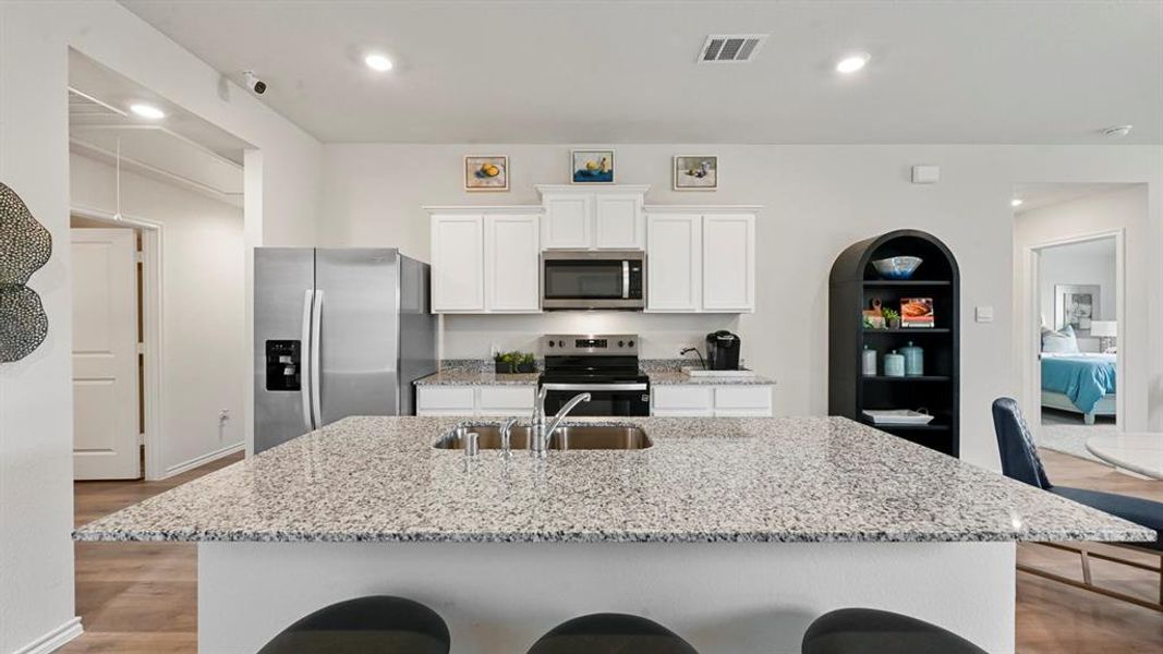 Kitchen featuring light stone countertops, appliances with stainless steel finishes, white cabinets, a center island with sink, and wood finished floors Kitchen featuring light stone countertops, appliances with stainless steel finishes, white cabinets, a center island with sink, and wood finished floors