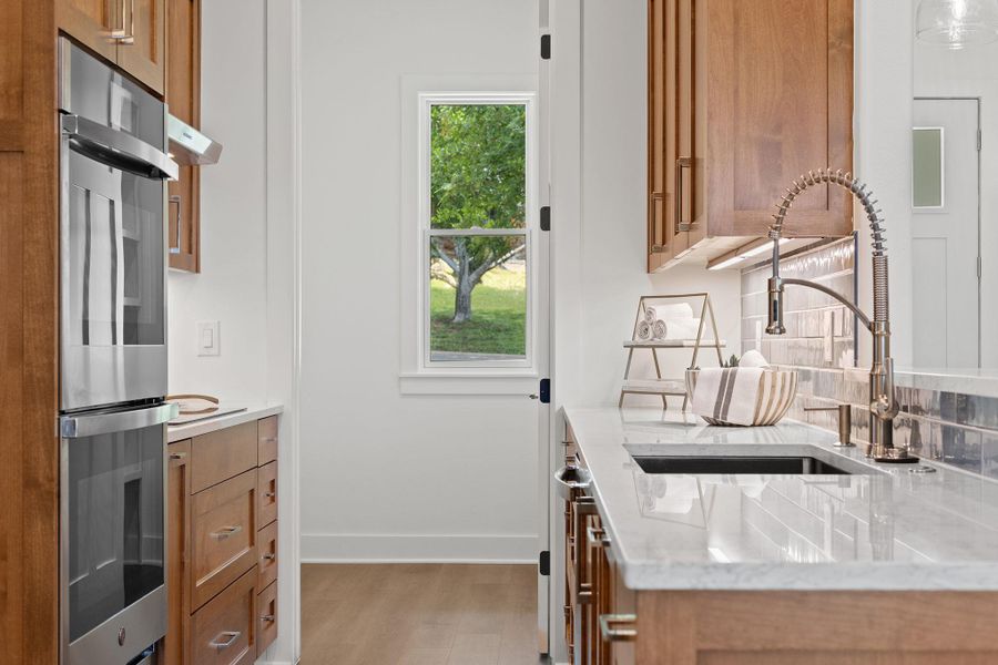 Kitchen featuring brown cabinetry, double oven, a sink, and wood finished floors Kitchen featuring brown cabinetry, double oven, a sink, and wood finished floors