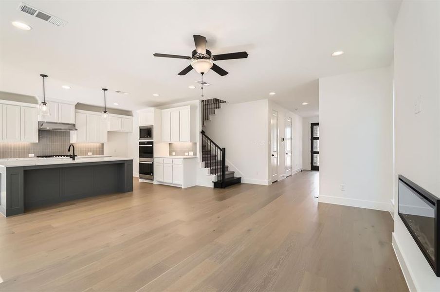 Kitchen featuring light hardwood / wood-style floors, a center island with sink, hanging light fixtures, backsplash, and white cabinetry