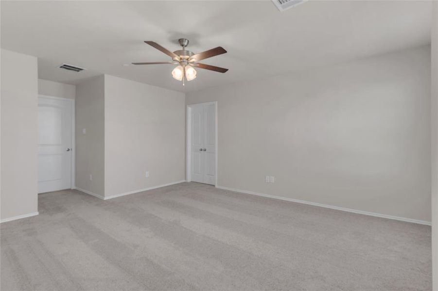 This is a spacious Primary bedroom, well-lit room with neutral walls and carpeting, featuring a ceiling fan with lights and central air conditioning vent.