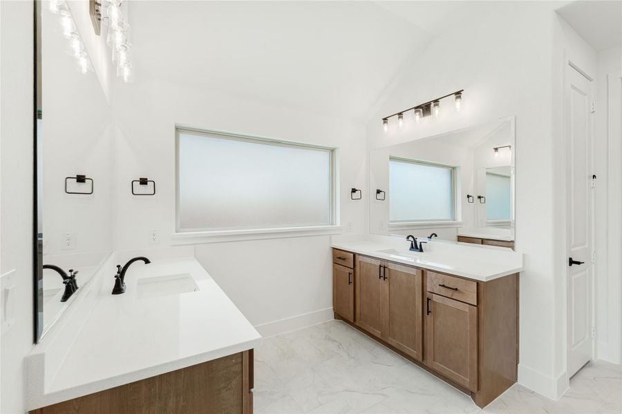 Bathroom with dual vanities, wood cabinets, white countertops, and marble tile floors Bathroom with dual vanities, wood cabinets, white countertops, and marble tile floors