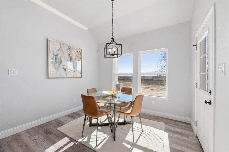 Dining space with vaulted ceiling, ornamental molding, light hardwood / wood-style floors, and a notable chandelier