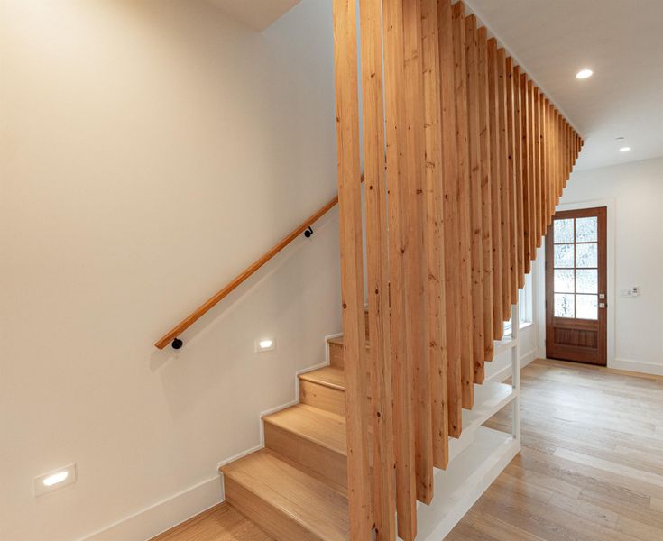 A striking modern staircase with light wood steps and vertical slat railings anchors this inviting entry. A striking modern staircase with light wood steps and vertical slat railings anchors this inviting entry.